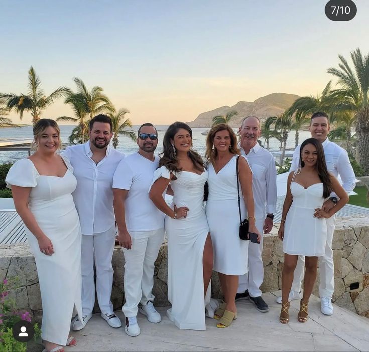 a group of people standing next to each other in front of palm trees and water