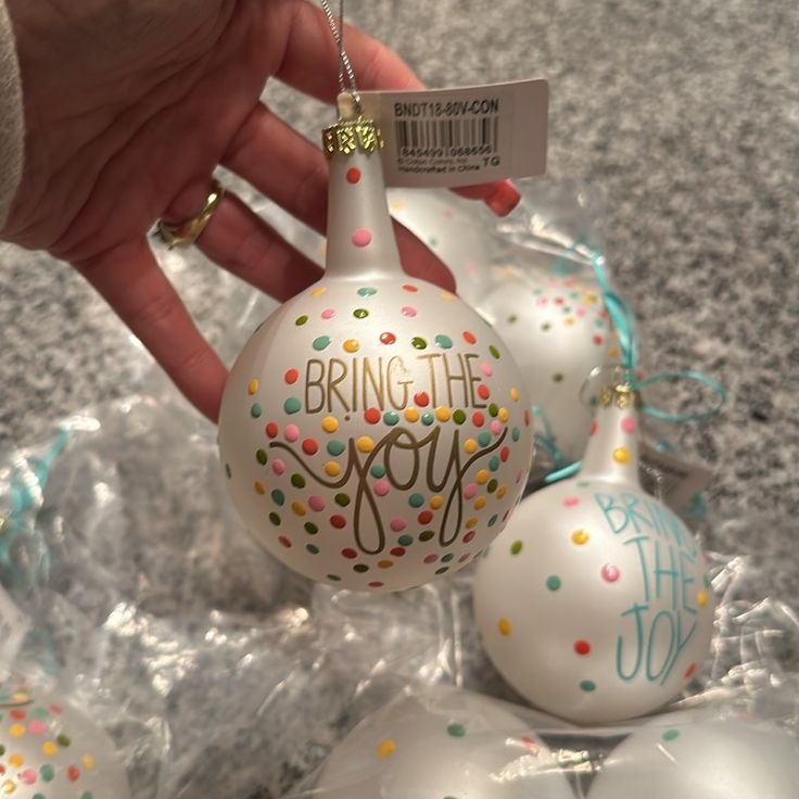 a hand is holding a white ornament that says bring the joy with confetti on it