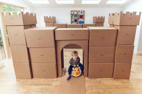 a young boy sitting on top of a cardboard castle with lots of boxes around him