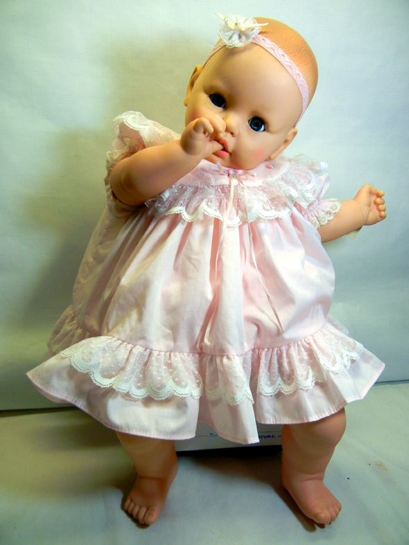 a baby doll wearing a pink dress and holding her hand up to her mouth with both hands