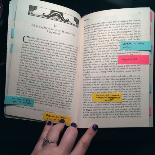 a person's hand holding an open book with sticky notes attached to the pages