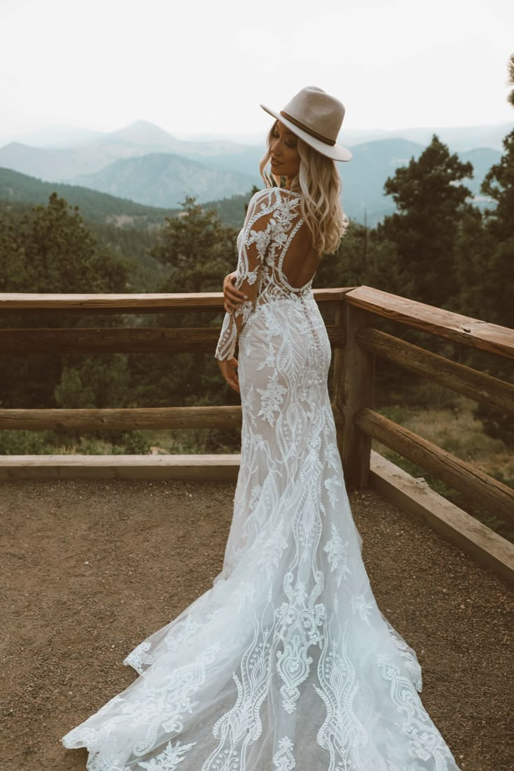 a woman standing on top of a wooden deck wearing a white wedding dress and hat