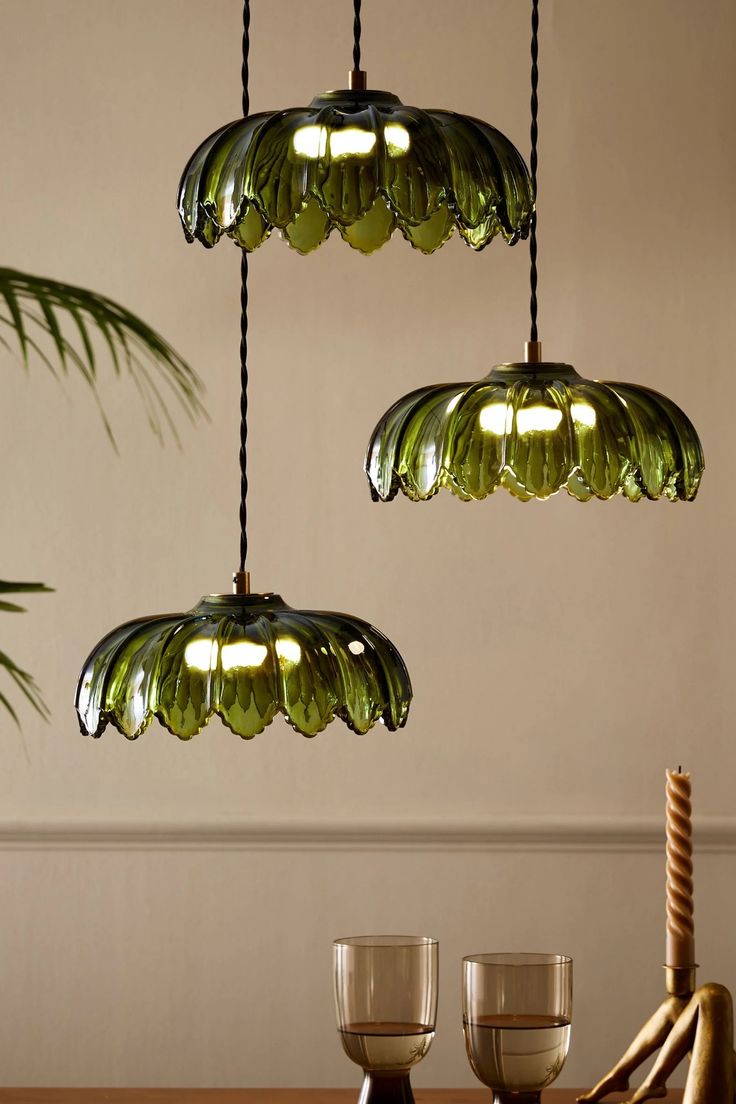 three green glass lights hanging from the ceiling above a wooden table with two wine glasses on it