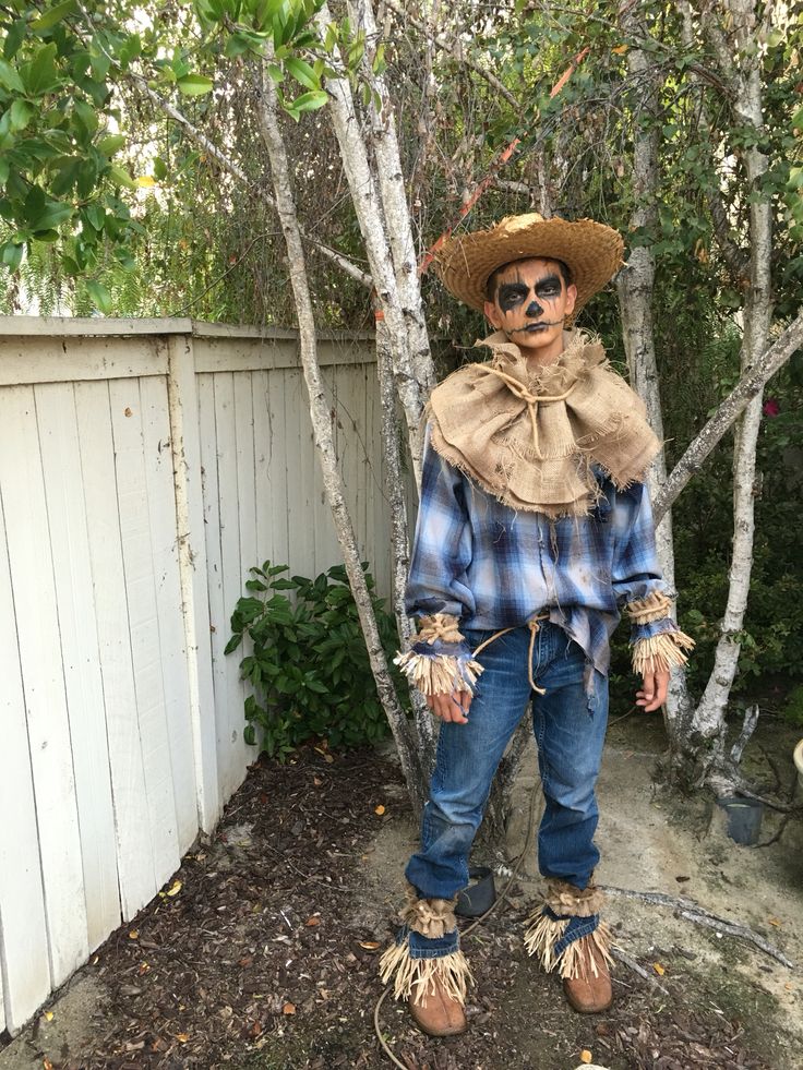 a scarecrow standing in front of a tree wearing sunglasses and a plaid shirt with tassels