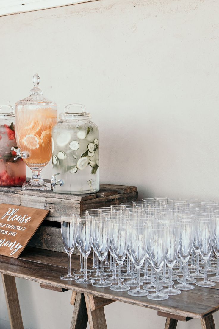 there are many wine glasses on the table with drinks in jars and glassware next to each other