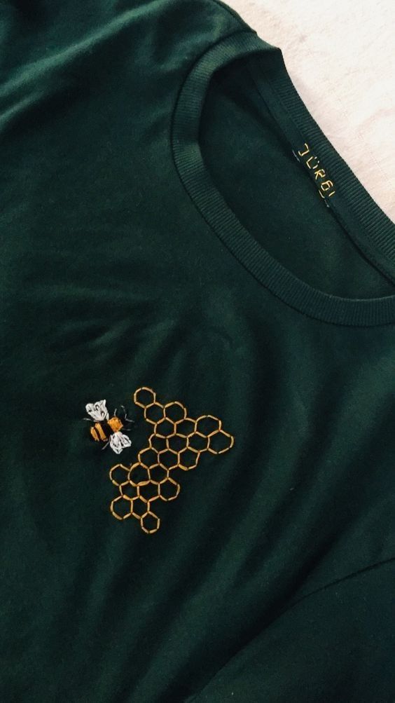 a green t - shirt with a bee and honeycomb embroidered on the chest, sitting on a white surface