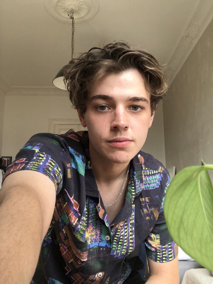 a young man is looking at the camera while holding a green plant in his hand