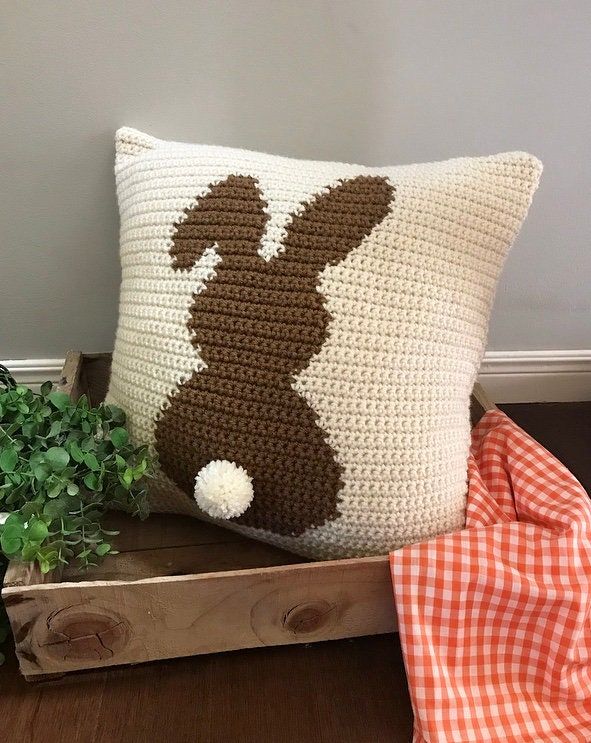 a crocheted bunny pillow sitting on top of a wooden crate next to a potted plant