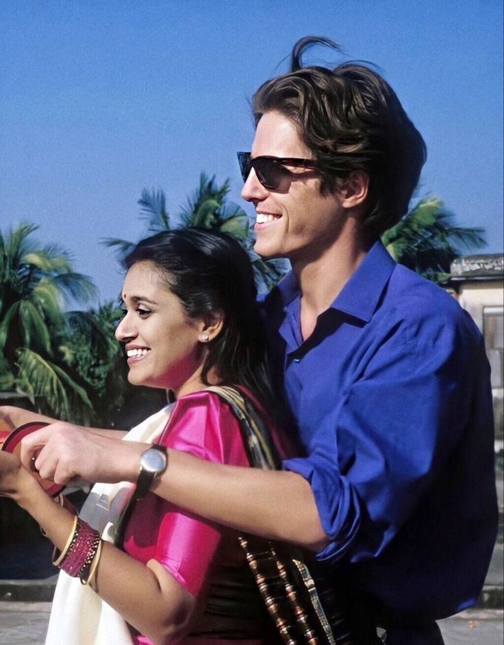 a man and woman standing next to each other in front of some palm trees with their cell phones