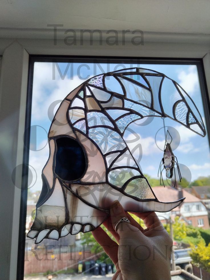 a hand holding up a glass mask in front of a window