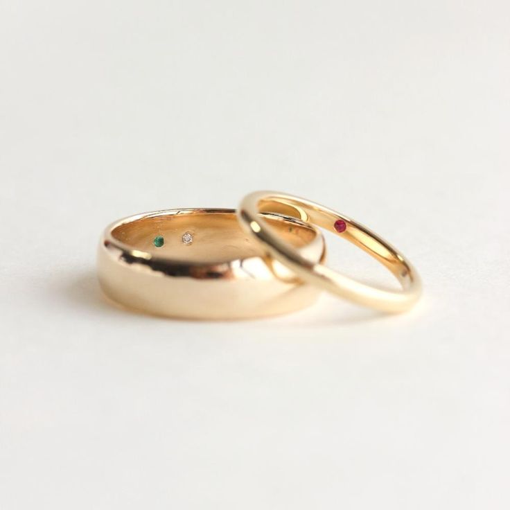 two gold wedding rings with different colored stones on each one, set against a white background