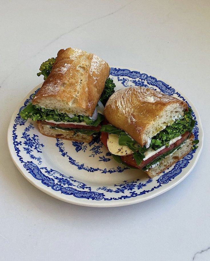 two sandwiches are sitting on a plate with blue and white trimmings, one is cut in half