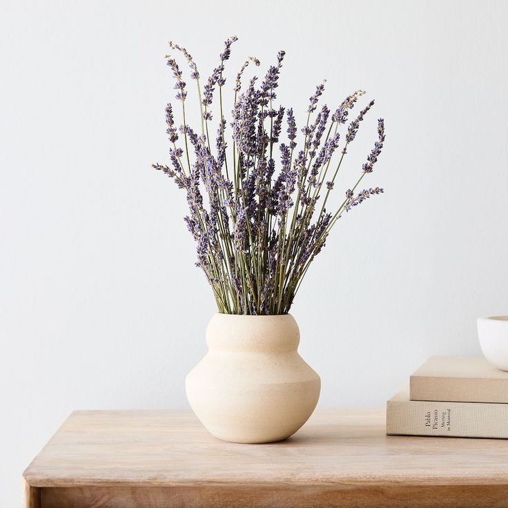 a white vase filled with purple flowers sitting on top of a table next to a stack of books