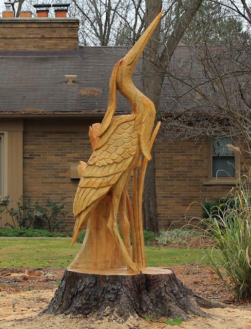 a statue of a bird on top of a tree stump in front of a house