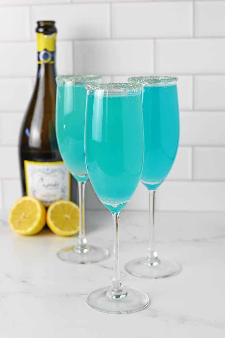 three glasses filled with blue liquid next to a bottle of wine on a counter top