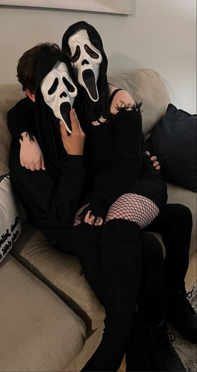 two people wearing masks sitting on a couch with one holding the other's face