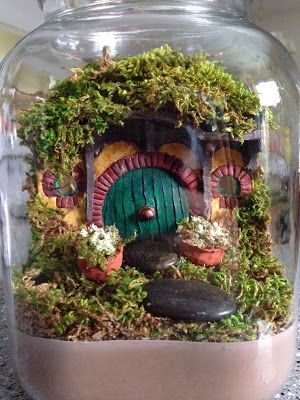 a glass jar filled with plants and a gnome's house in the bottom half