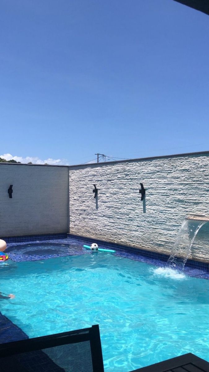 an outdoor swimming pool with blue water and people playing in the water, on a sunny day