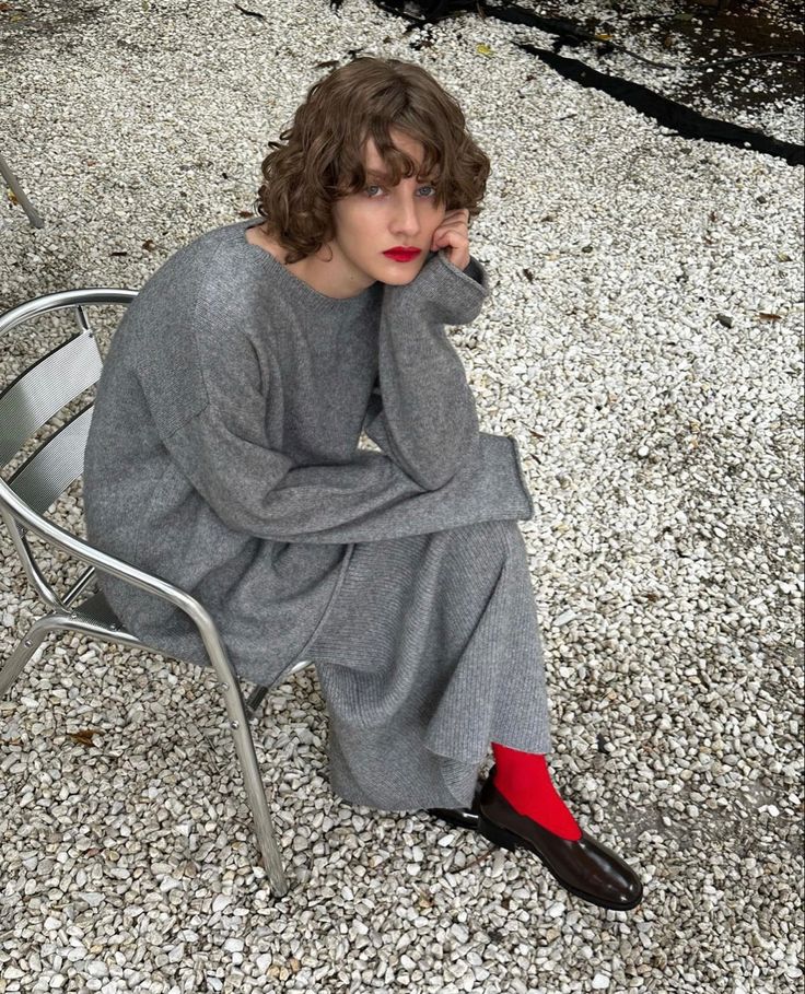 a woman sitting on top of a metal chair next to a white wall and red socks