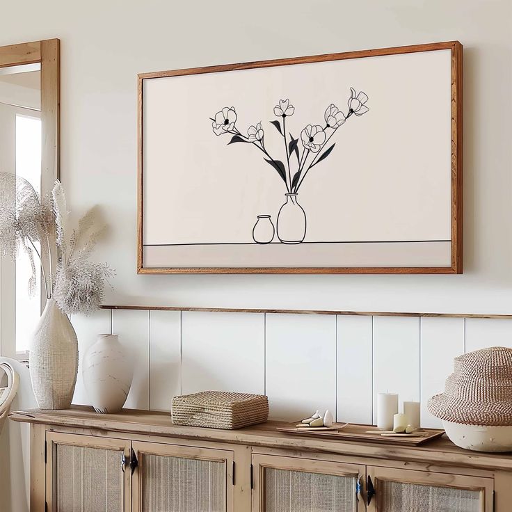 a painting hanging on the wall next to a wooden cabinet with vases and flowers