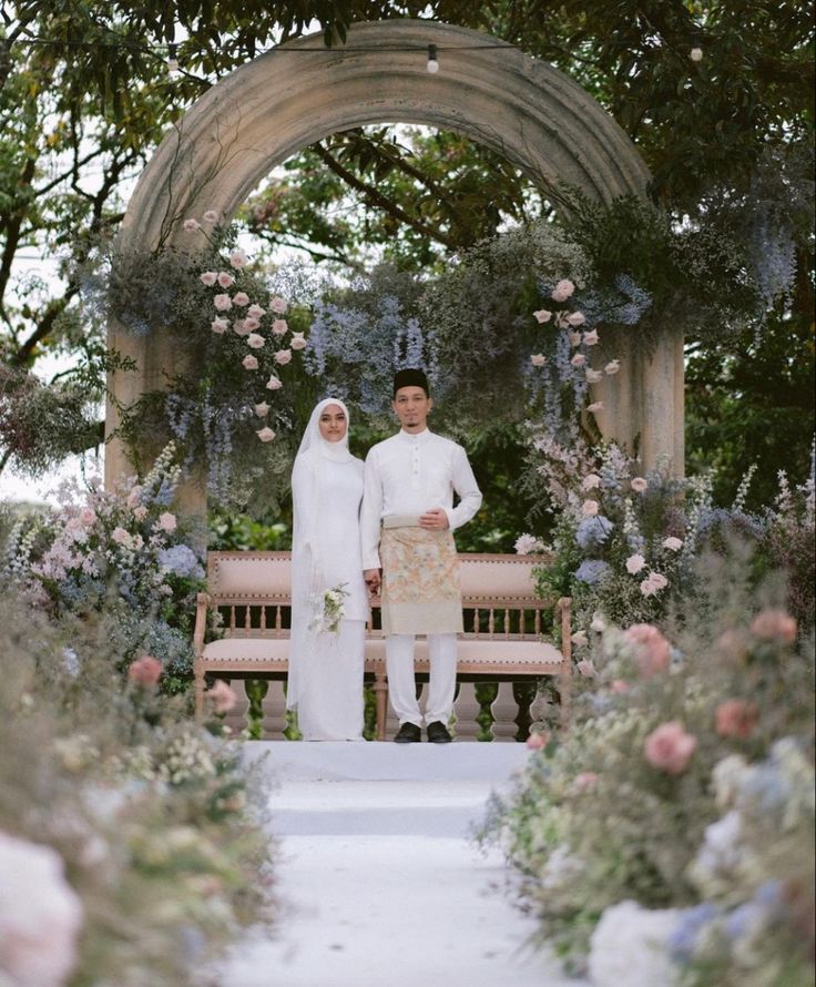 two people standing next to each other in front of a bench with flowers on it