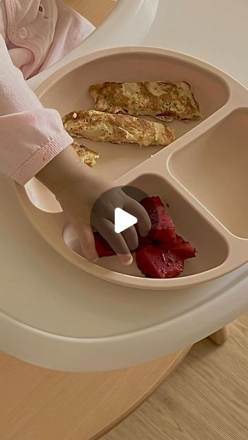 a baby sitting in a highchair eating food from a tray on top of a table