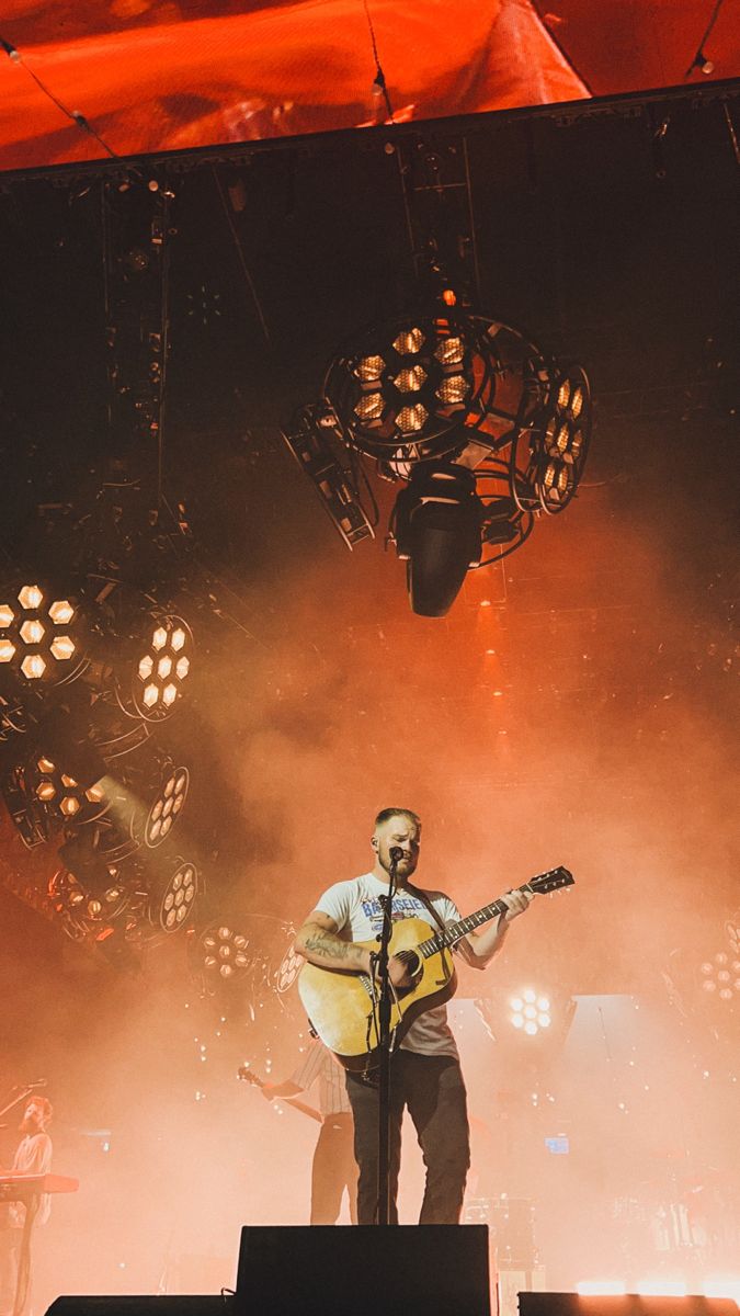 a man standing on top of a stage with a guitar in his hand and lights behind him