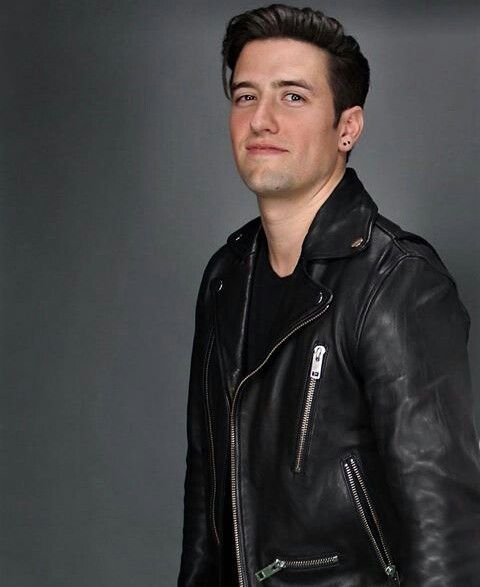 a man in a black leather jacket is posing for the camera with his hand on his hip