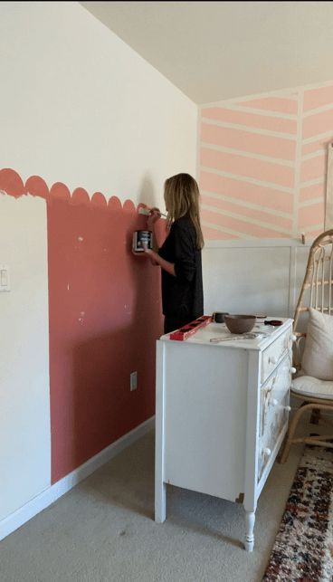 a woman is painting the wall in her bedroom with pink and white stripes on it