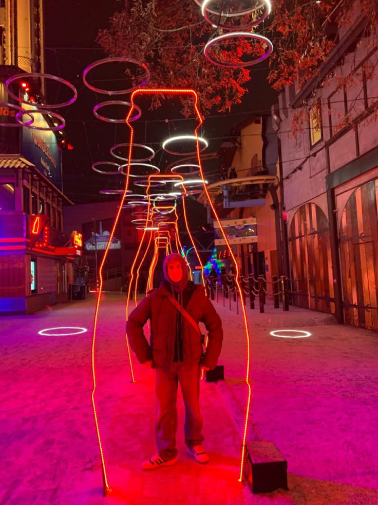 a man standing in the middle of a street at night with neon lights all around him