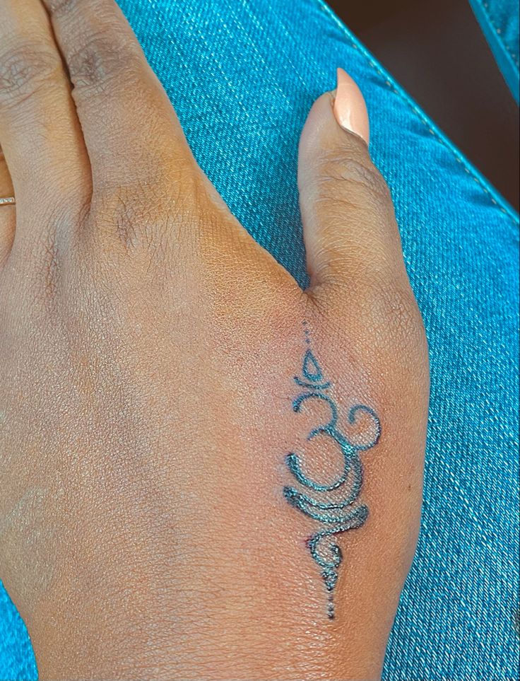 a woman's hand with a small tattoo on her left wrist and the word om written in silver ink