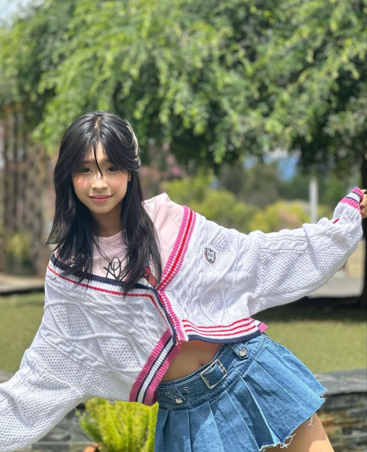 a girl in a white shirt and blue skirt posing for the camera with her hand on her hip