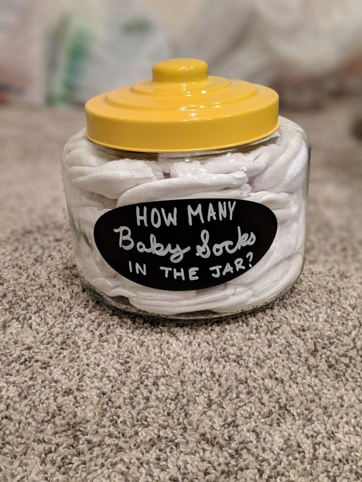 a glass jar filled with white baby socks on top of a carpeted floor next to a plastic yellow lid