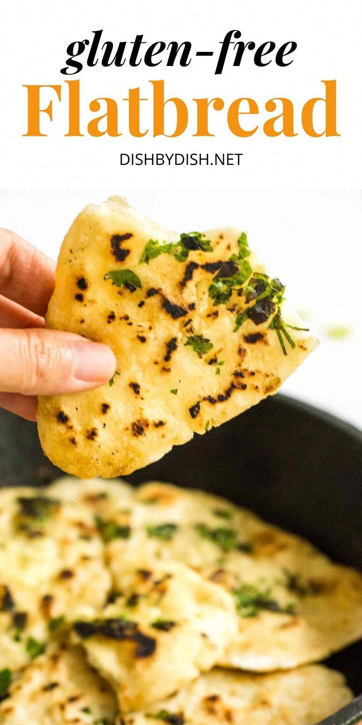 a hand holding up a piece of flatbread over a skillet filled with cheese and herbs