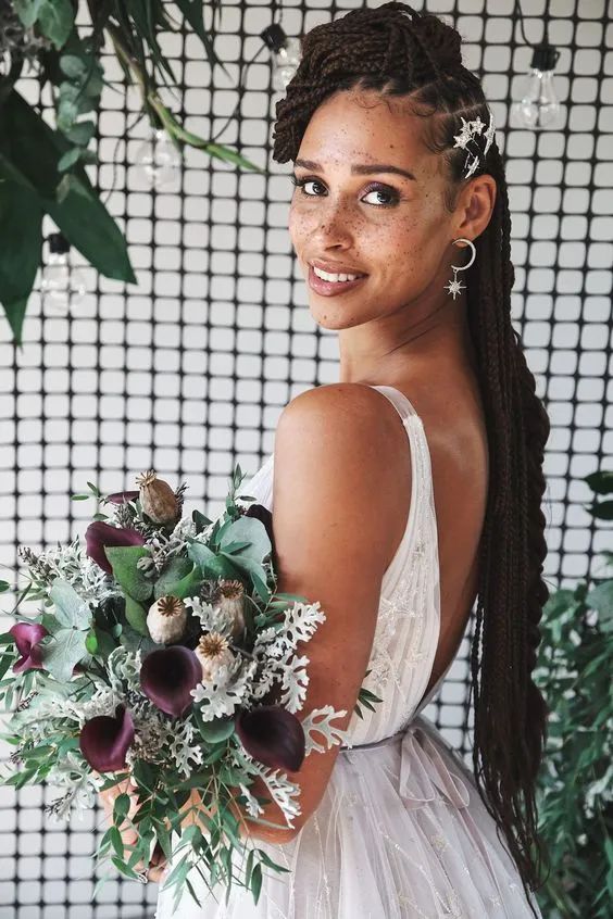 a woman in a white dress holding a flower bouquet and smiling at the camera with greenery behind her