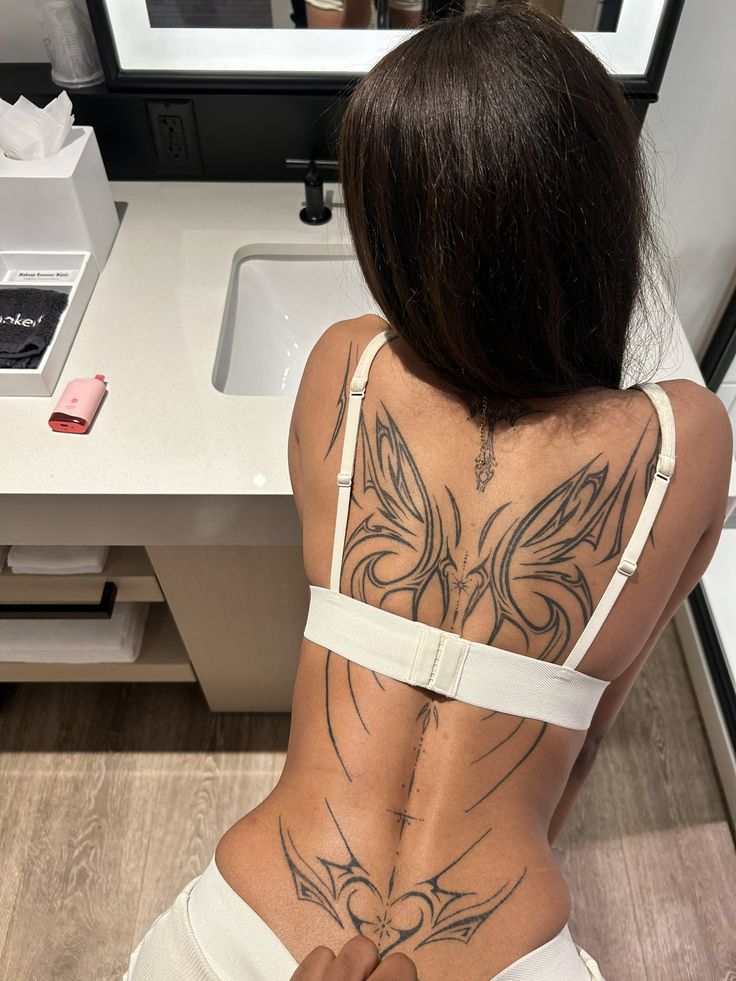 a woman with tattoos on her back sitting in front of a sink