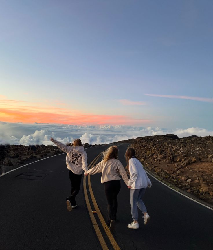 three people are walking down the road with their arms in the air as the sun sets