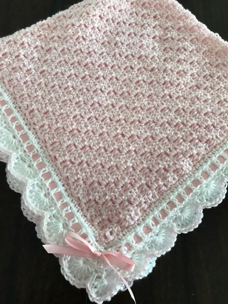 a pink and white crocheted blanket on top of a wooden table