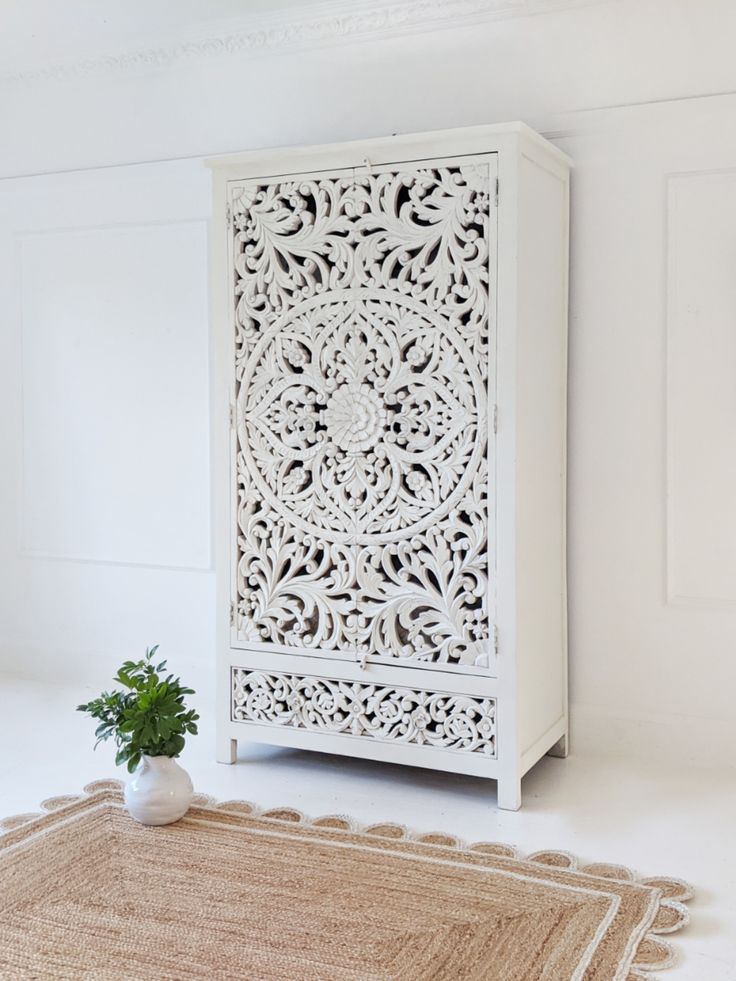 a white cabinet sitting on top of a rug next to a potted plant