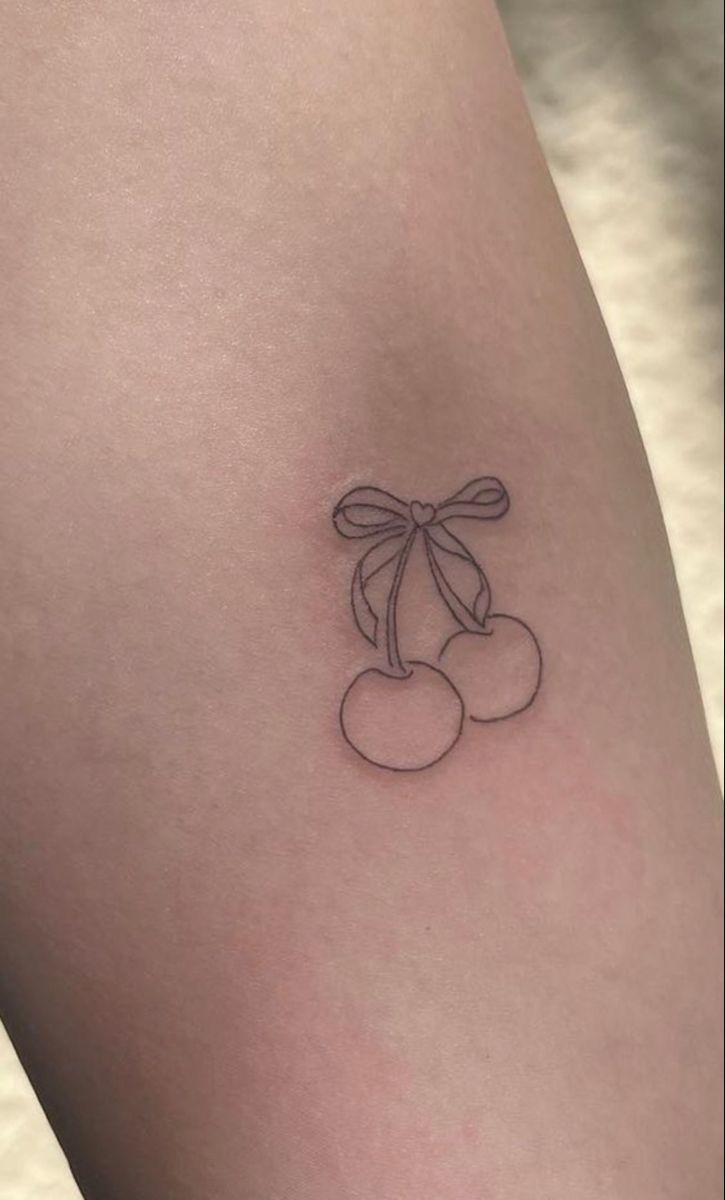 a small cherry tattoo on the thigh with a bow around it's neck and two cherries