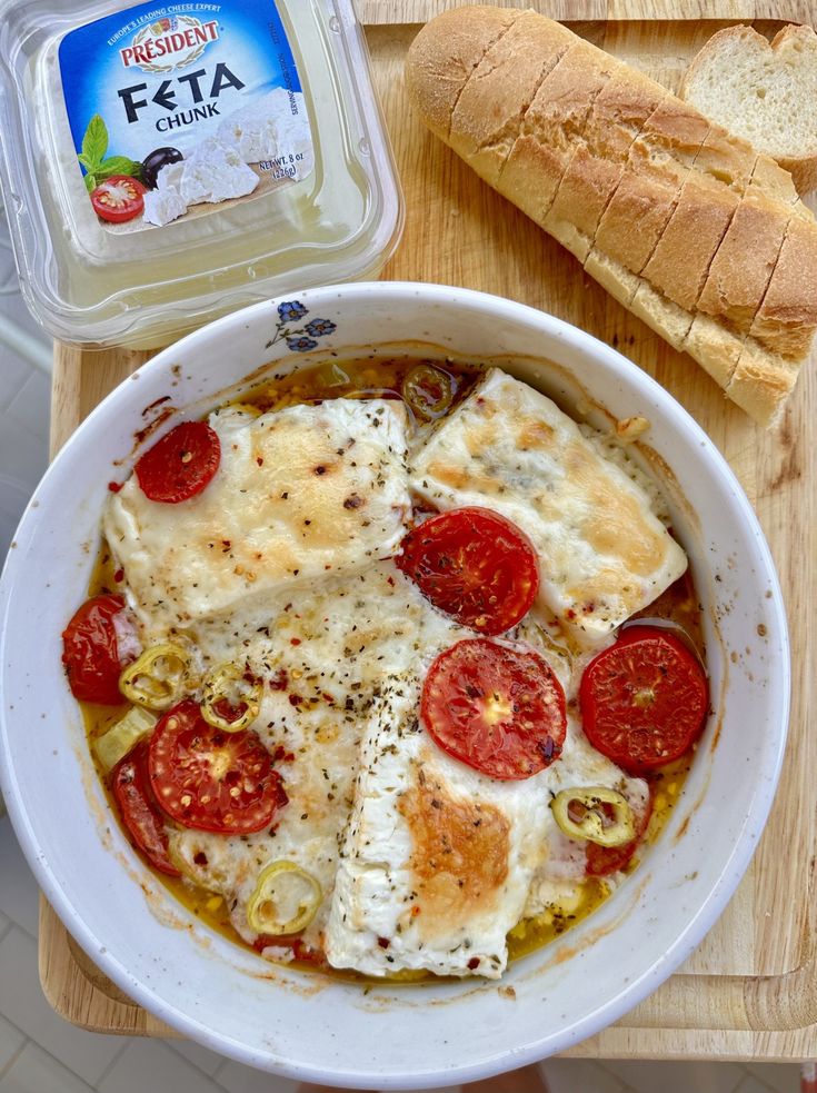 a white bowl filled with food next to a loaf of bread on top of a wooden cutting board