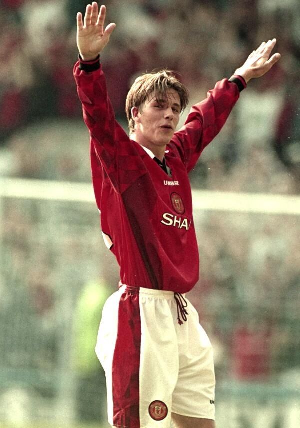 a young man in red and white uniform holding his arms up to the air while standing on a soccer field