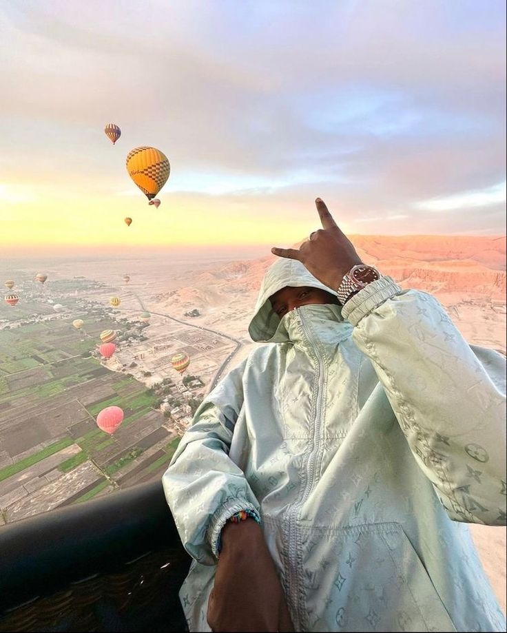 a man is looking out at hot air balloons in the sky as he holds his finger up