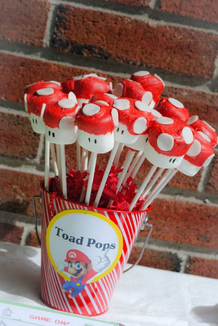 red and white cake pops in a bucket on a table next to a brick wall