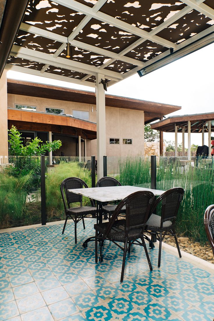 an outdoor dining table and chairs under a pergolated roof with grass in the background