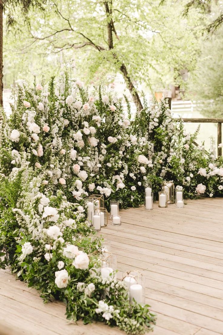 white flowers and candles are lined up on a wooden deck in front of some trees