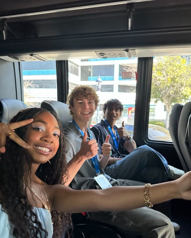 three people sitting in the back of a bus with their thumbs up and one person standing next to them