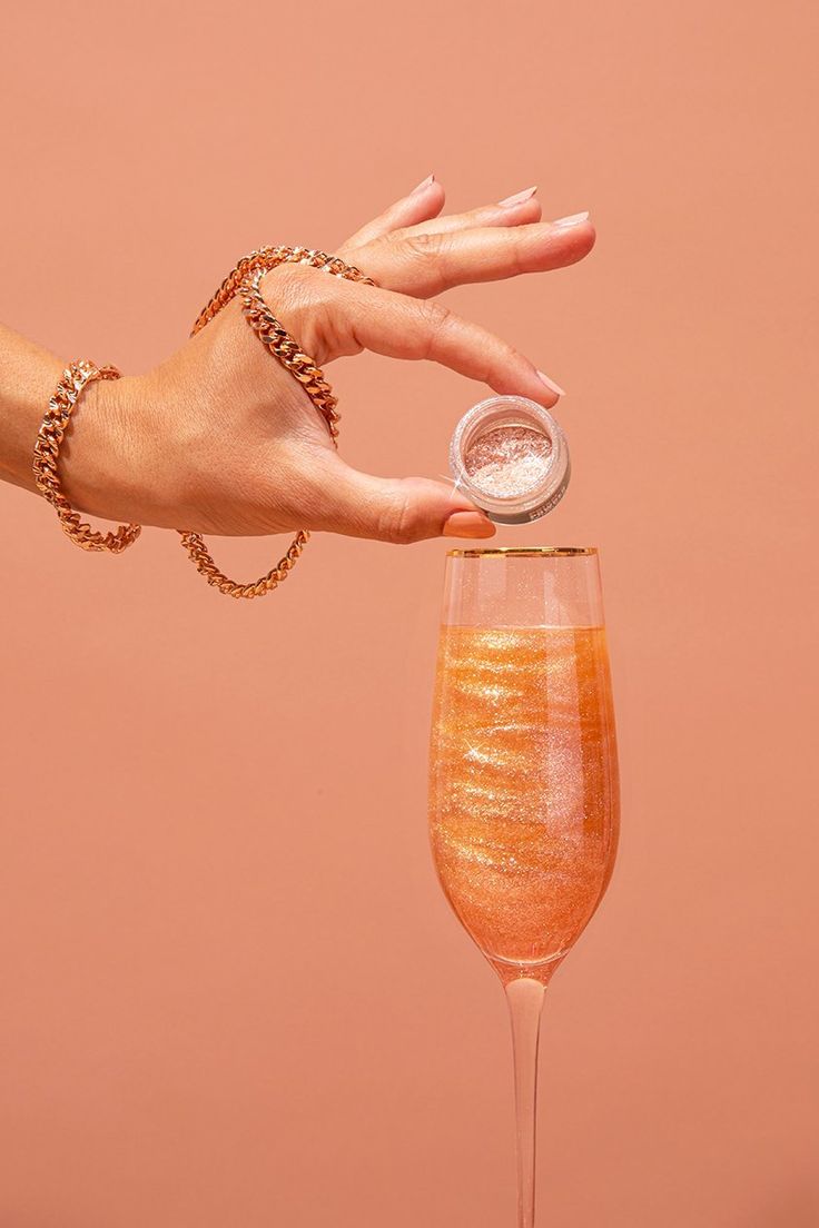 a hand is holding a glass with some liquid in it and an orange substance on the rim