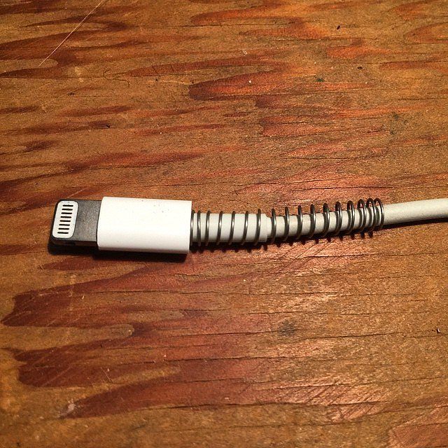 an iphone charger plugged into the side of a wooden table with a white cord