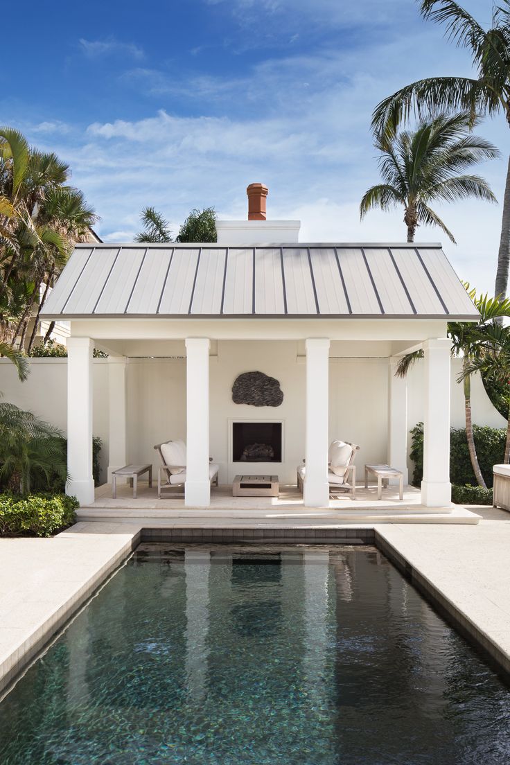 a pool house with an outdoor fireplace and seating area next to the pool is surrounded by palm trees